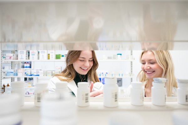 Two pharmacists looking at medications on a shelf in a pharacy